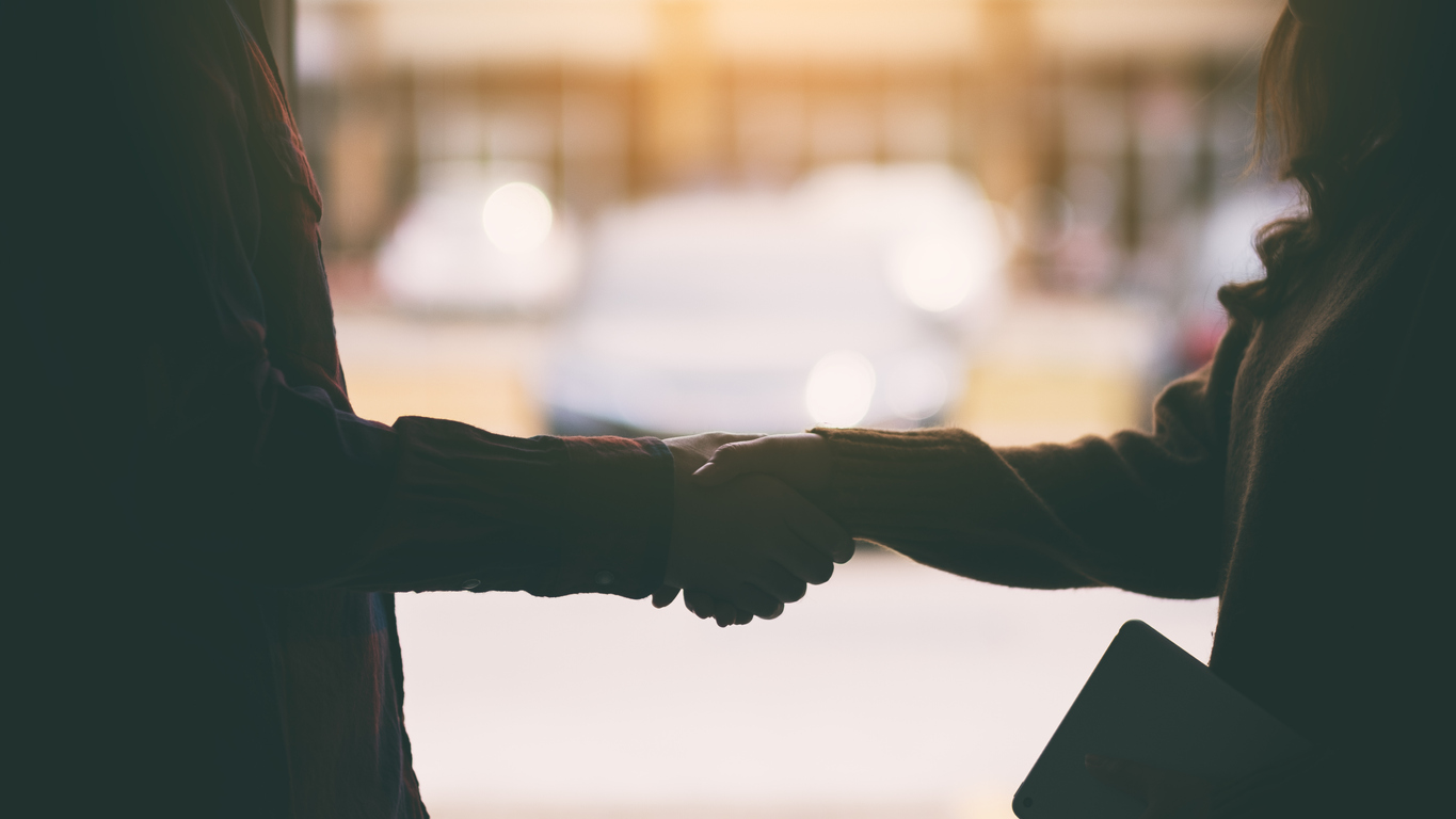 Silhouette image of two people shaking hands